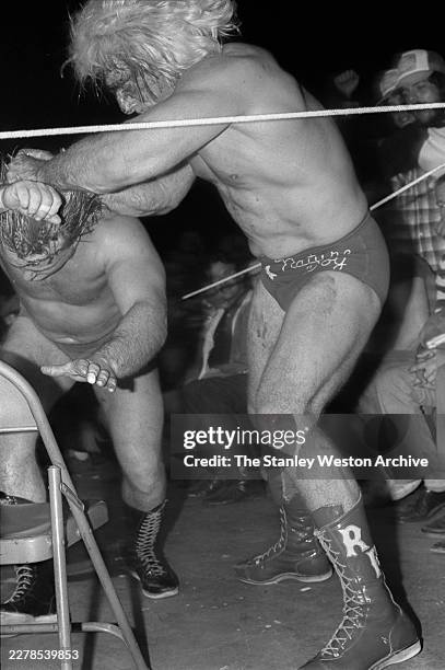 American professional wrestler Greg Valentine's head is brought down onto a chair by American professional wrestler Ric Flair during a professional...