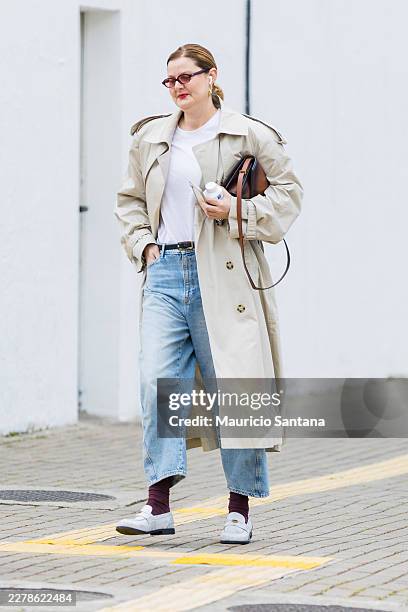 Guest wears brown hair, pulled back, tortoiseshell sunglasses, white t-shirt, beige trench coat, double-breasted, light blue wide-leg jeans, high...