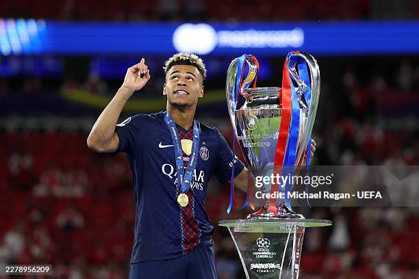Desire Doue of Paris Saint-Germain gestures to the sky as he walks past the UEFA Champions League trophy after his team's victory in the UEFA...