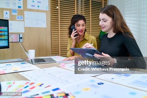 Ui/ux designers collaborating on user interface development, discussing mobile application design with a tablet, laptop, and color palettes on an office desk Ui/ux designers collaborating on user interface development, discussing mobile application design with a tablet, laptop, and color palettes on an office desk