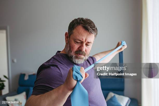 mature man exercising at home, using resistance band. - chronic illness stock pictures, royalty-free photos & images