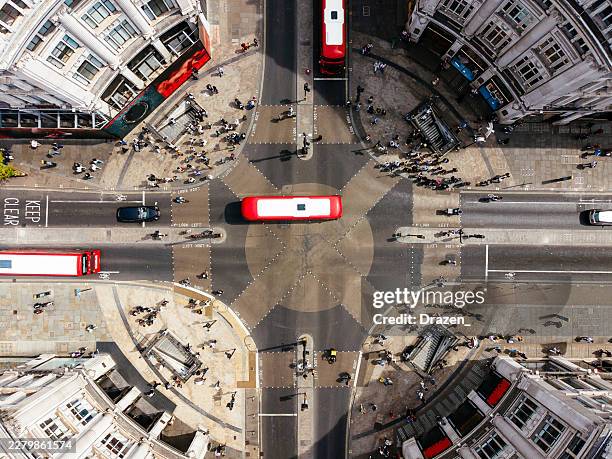 an overhead shot of a bustling city intersection featuring red double-decker buses, pedestrians, and surrounding buildings. - central london stock pictures, royalty-free photos & images