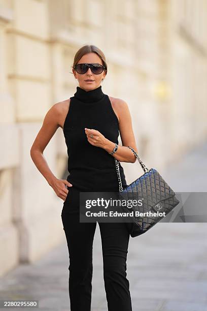Diane Batoukina wears brown hair with a center part pulled back into a low bun, black oversized sunglasses with dark lenses by Kaleos, a black fitted...