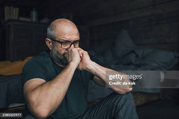 middle-aged man sitting alone on floor in bedroom holding face, sad and reflective moment - hopelessness stock pictures, royalty-free photos & images