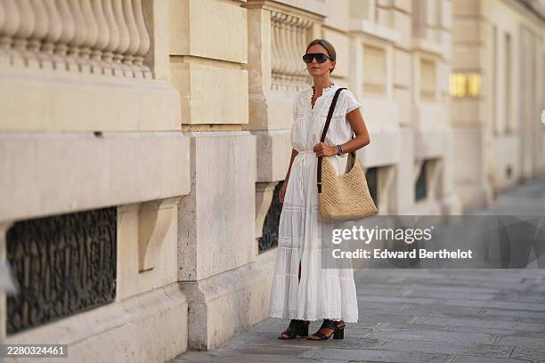 Diane Batoukina wears light brown hair with a center part pulled into a low bun, black oversized square sunglasses, a white cotton short-sleeve...
