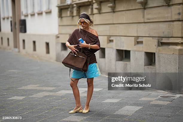 Julia Kammerer is seen wearing a dark brown draped jersey top with an off shoulder neckline and gathered side detailing from NA KD; light blue...