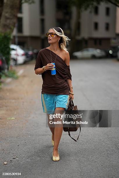 Julia Kammerer is seen wearing a dark brown draped jersey top with an off shoulder neckline and gathered side detailing from NA KD; light blue...