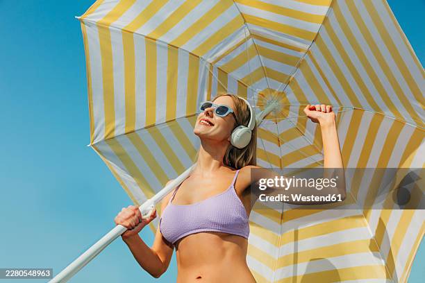 smiling woman in swimsuit enjoying music by umbrella on summer vacation - mid adult women stock pictures, royalty-free photos & images