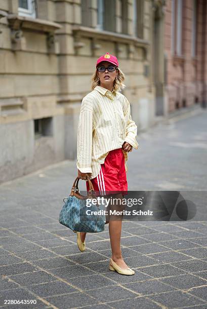 Julia Kammerer is seen wearing an oversized cream cotton striped button front shirt with patch pocket details from Pull&Bear; red cotton shorts with...