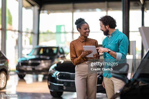 car salesperson helping a customer purchasing a vehicle while using a tablet in a showroom - auto loan stock pictures, royalty-free photos & images