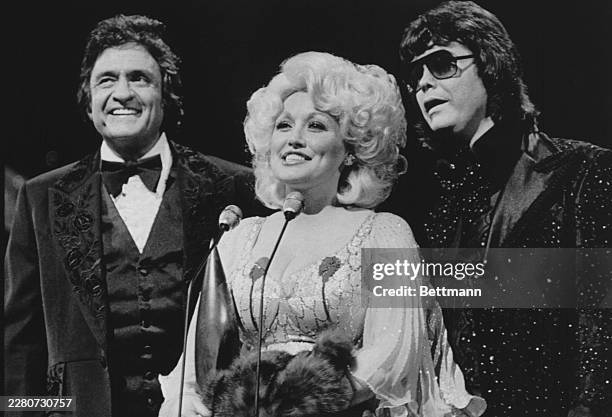 Flanked by Johnny Cash, , and Ronnie Milsap, Dolly Parton accepts the Entertainer of the Year award during the Country Music Association awards.