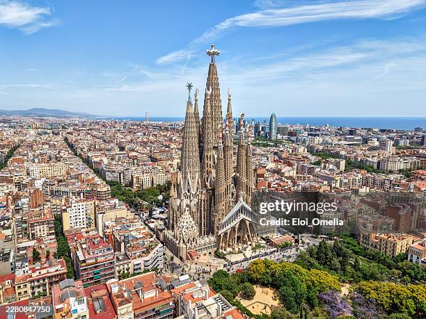 sagrada familia rising above barcelona's urban expanse, highlighting gaudí's ornate basilica, surrounding rooftops and the distant blue mediterranean on a clear sunny day - sagrada família imagens e fotografias de stock