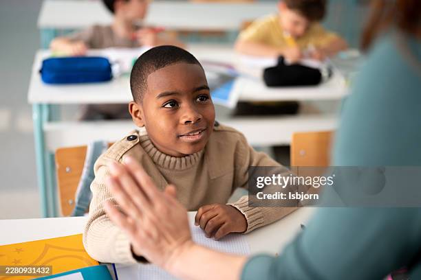 teacher giving high five to happy schoolboy in classroom. - encouragement stock pictures, royalty-free photos & images