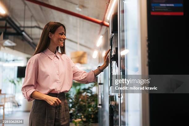 employee buying snack from vending machine during break - office vending machine stock pictures, royalty-free photos & images