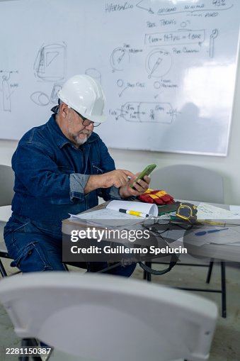 Engineer using smartphone while working on hyperbaric chamber plans Engineer using smartphone while working on hyperbaric chamber plans