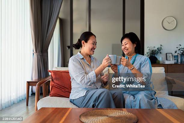 mother and daughter sharing tea on home sofa - familie met twee generaties stockfoto's en -beelden