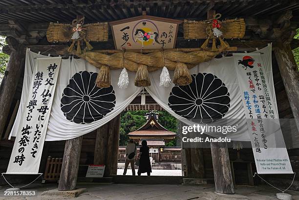 Spiritual pilgrims walk through a massive wooden torii gate to ascend the forest-lined stone steps leading into the main sanctuary of Kumano Hongu...