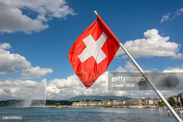 Swiss flag waves proudly near Jet d'Eau on Lake Geneva in Geneva canton under a clear sky. Switzerland.