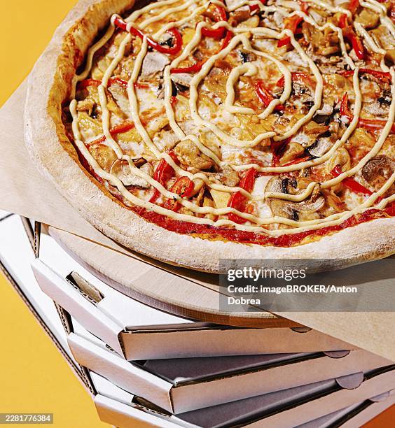 food, a vibrant pizza featuring red peppers, mushrooms, and sauce is displayed atop a tall stack of white pizza boxes. the bright yellow background enhances the appetizing appearance - pizza boxes stack stock pictures, royalty-free photos & images