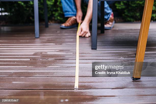 person measures wet outdoor terrace planks using yellow tape measure. composite decking installation, eco friendly patio renovation, outdoor wood plastic composite. - libelle stock-fotos und bilder