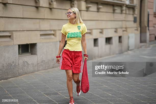 Julia Kammerer is seen wearing a yellow popcorn fabric short sleeve top with Brazil print from Pull & Bear; red athletic shorts from Adidas; red and...