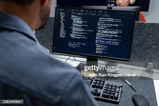 Asian Male Software Developer Reviewing Source Code on Screen, Typing on a Keyboard During an Active Coding and Program Development Session. Asian Male Software Developer Reviewing Source Code on Screen, Typing on a Keyboard During an Active Coding and Program Development Session.