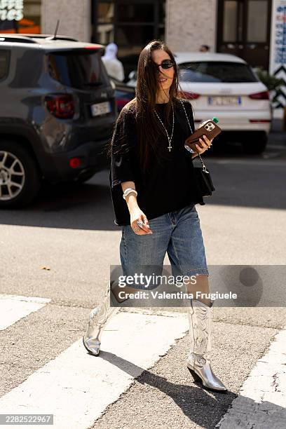 Guest wears black sunglasses, a black t-shirt, denim bermuda shorts, silver knee high heeled cow boy boots, a black leather crossbody bag and a...