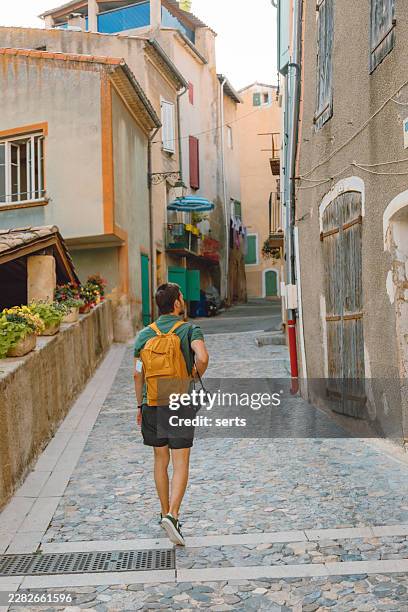 young tourist man looking around while walking through a historic alley in valensole, provence, france - cobblestone stock pictures, royalty-free photos & images