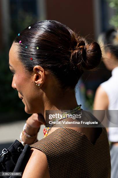 Guest wears rhinestones in the hair, beaded necklaces, a black bag and a beige checked sleeveless to outside Simon Cracker show during the Milan...