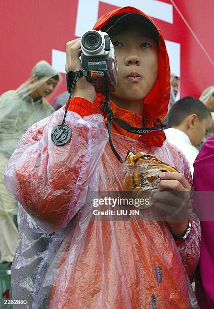 Girl wearing a raincoat, videos the Real Madrid training session at Hongta sports center in the southwestern city of Kunming, 26 July 2003. The Real...