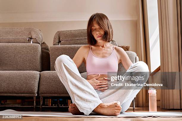 woman meditating on yoga mat at home, hands on abdomen - exhaling stock pictures, royalty-free photos & images