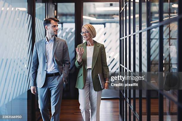 two business persons walking side by side while having a discussion - walking side by side stock pictures, royalty-free photos & images