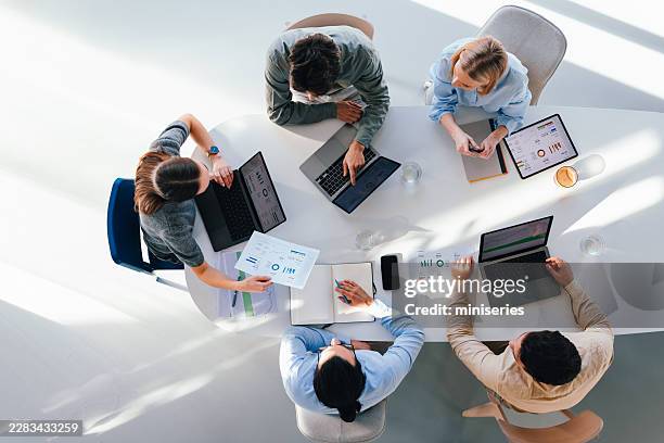 top-view business team meeting around table with laptops and documents collaborating on data - round table top stock pictures, royalty-free photos & images
