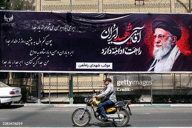 Man rides a motorcycle past a mourning banner depicting Iran's slain supreme leader Ali Khamenei, who was killed in a strike on the first day of the...