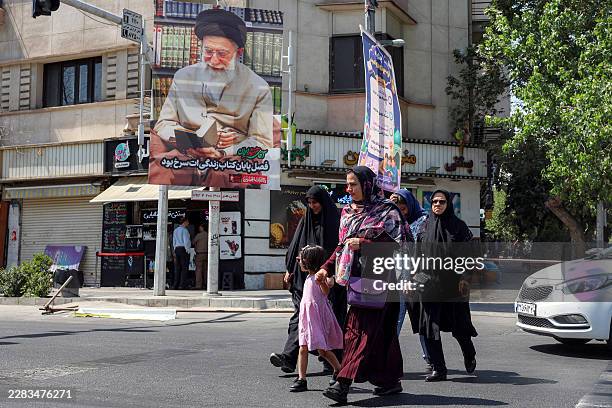 Women cross a street past a mourning billboard depicting Iran's slain supreme leader Ali Khamenei, who was killed in a strike on the first day of the...
