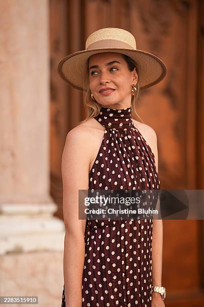 Nina Meise is seen wearing a sleeveless brown midi dress from Zara and a beige wide-brim hat from Mayser. She accessorizes the look with gold-tone...