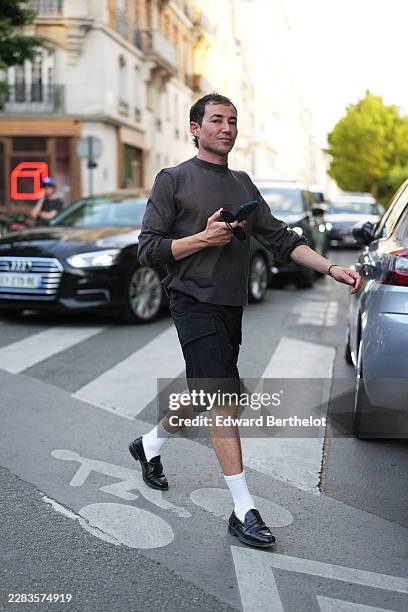 Guest wears short dark brown hair, a charcoal gray sweatshirt, black cargo shorts, white socks, black shiny varnished leather loafers shoes, outside...