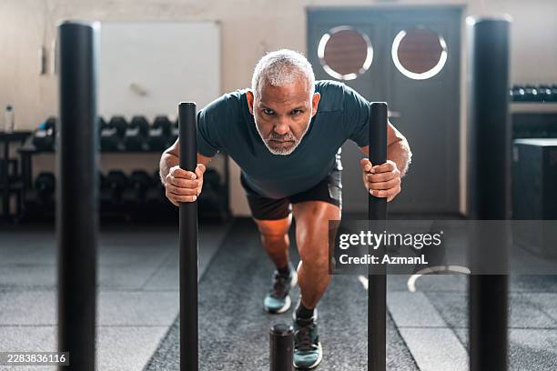 senior hispanic male driving weighted sled forward with concentrated intensity in gym - handle stock pictures, royalty-free photos & images