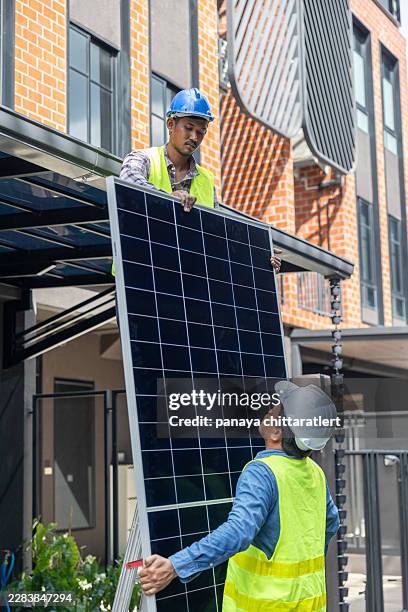 solar panel installation.technicians carrying solar module while installing solar panel system on roof of house .professional team worker installing solar panels on the roof of a house - solar module stock pictures, royalty-free photos & images