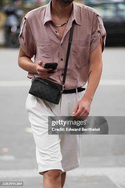 Guest wears a pink short-sleeve shirt, white knee-length shorts, a black shiny leather belt, a black monogram print pattern in coated canvas...