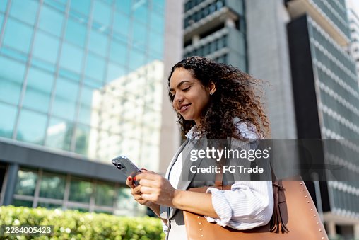 Geschäftsfrau im mittleren Erwachsenenalter, die ein Mobiltelefon benutzt und in der Stadt spazieren geht Geschäftsfrau im mittleren Erwachsenenalter, die ein Mobiltelefon benutzt und in der Stadt spazieren geht