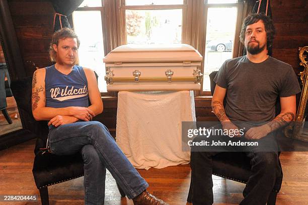 Portrait of American Rock musicians Jonathan Terrell and Wes Cargal, both of the duo Not in the Face, as they pose on either side of a casket,...