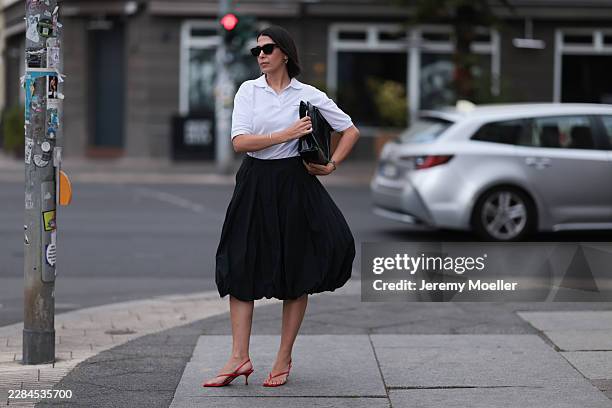 Tugba Kement is seen wearing sleek dark shoulder-length hair with a center part, slim black Saint Laurent sunglasses, small silver earrings, a white...