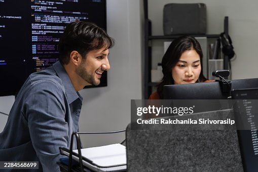 Software developer typing source code at office workstation, working with multiple monitors and development tools to support programming, debugging, and efficient software workflow. Software developer typing source code at office workstation, working with multiple monitors and development tools to support programming, debugging, and efficient software workflow.