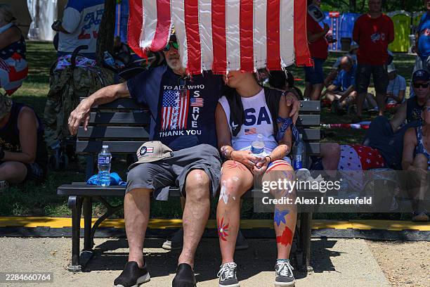 Person holds an American flag over people to create shade on a bench at The Great American State Fair along the National Mall on July 04, 2026 in...