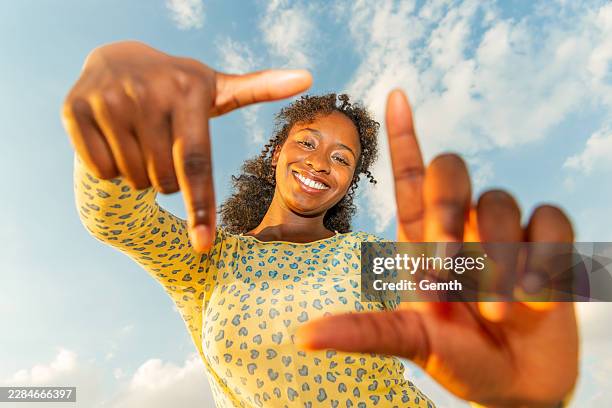 happy black woman framing future vision with hands against sky at golden hour - the bigger picture stock pictures, royalty-free photos & images