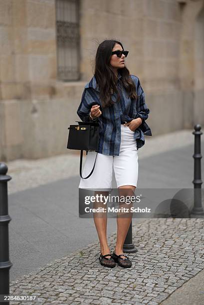 Aylin Sengül is seen wearing an oversized navy blue striped button-up shirt by Massimo Dutti; white knee-length denim Bermuda shorts by COS; black...