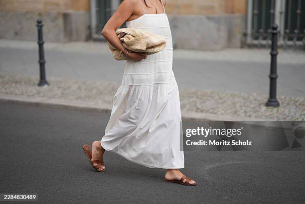 Aylin Sengül is seen wearing a white spaghetti-strap maxi dress with textured horizontal panels and a gathered hem by COS; brown leather “Oran”...