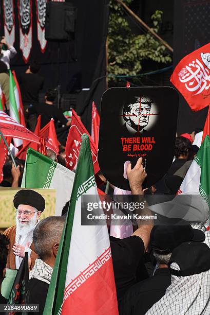People gather and hold up a Image of Donald Trump with a messages of "There will be blood" as they bid the last farewell to Iran's Supreme Leader...