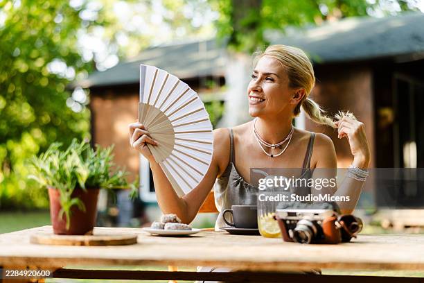 femme profitant de l’après-midi d’été avec un éventail et un café dehors - éventail photos et images de collection